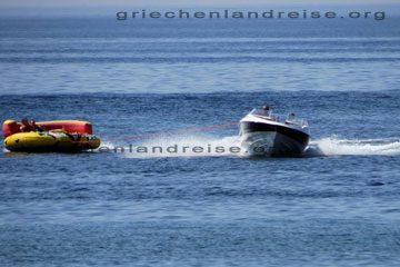 Touristen die sich beim Griechenland Urlaub auf der griechischen Insel Korfu in einem kreisrunden Schlauchboot sitzend von einem Motorboot in der Nähe vom Strand entlang gezogen werden.
