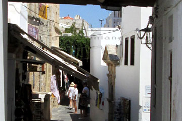 Touristen beim bummeln durch die schmalen Gassen von Lindos auf der Insel Rhodos beim Griechenland Urlaub. Viele Souvenirs und Tavernen in den engen Gässchen in Lindos und Schatten spendende Dächer die über die Gassen gebaut sind.
