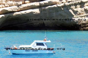 Die Motoryacht Daily Cruise in der Bucht von Matala vor Anker. Im Hintergrund Schwimmer, die in der Bucht von Matala vor der Felswand wo die Höhlen von Matala sind, im Meer baden. Auf der Insel Kreta in Griechenland.