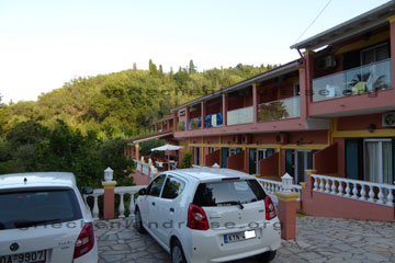 Auf dem Bild erkennt man die Ansicht vom Hotel Penelope mit den Balkonen und den Parkplatz davor wo man den Mietwagen parken kann in dem Ort Boukari auf der griechischen Insel Korfu.