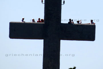 Eine Reisegruppe bei einem Ausflug zu einem Aussichtspunkt auf der Insel Rhodos. Hier auf dem Bild zu sehen, Touristen die hinter dem Querbalken von einem überdimensionalen Kreuz stehen und Bilder machen, das riesige Kreuz ist Teil von einer großen Klosteranlage.