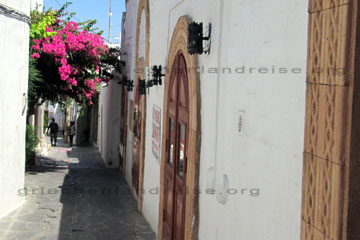 Schmale Gasse in Lindos mit farbenprächtigen Blumen und alten Portalen auf der Insel Rhodos in Griechenland.