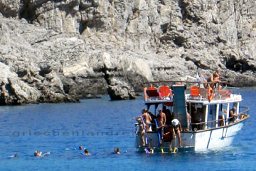 Touristen bei einer Schnorchel-fahrt auf der Insel Rhodos beim Griechenland Urlaub. Im Hintergrund die steile und graue Felsküste.