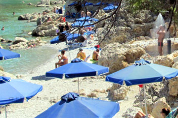Ein Badegast an einem Strand auf der griechischen Insel Rhodos der gerade unter der Dusche steht und sich abbraust nachdem er im Meer geschwommen ist um das Meersalz von der Haut zu bekommen. Das haben die Griechen gut gemacht die Duschen zwischen den Felsblöcken am Strand zu integrieren.