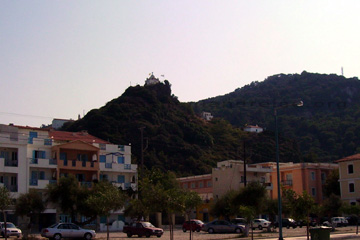 Anblick von dem kleinen Kloster auf der Bergspitze in Karlovassi auf der griechischen Insel Samos. Im Vordergrund ein Parkplatz vor etwas größeren Hotels.