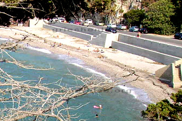 Parkende Autos an einem der Strände auf der Insel Samos. Im Vordergrund Schwimmer am Strand und man erkennt die Kaimauer samt den Treppen. In etwa 16 Stufen.