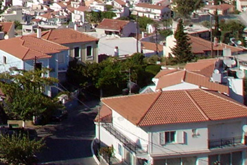 Straße und Häuser in dem Ortsteil Vathi auf der Insel Samos. Links und Rechts am Straßenrand Obstbäume die im Frühjahr blühen. Hier auf dem Bild war es aber Sommer.